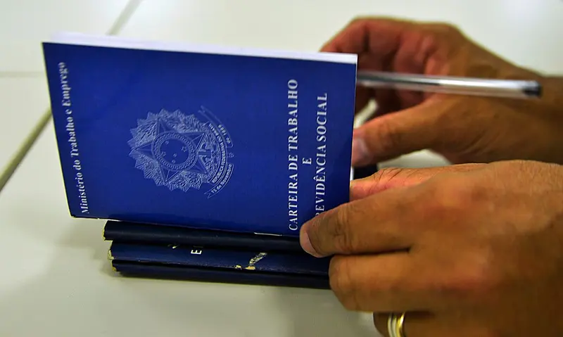 Mãos seguram carteiras de trabalho azuis sobre uma mesa