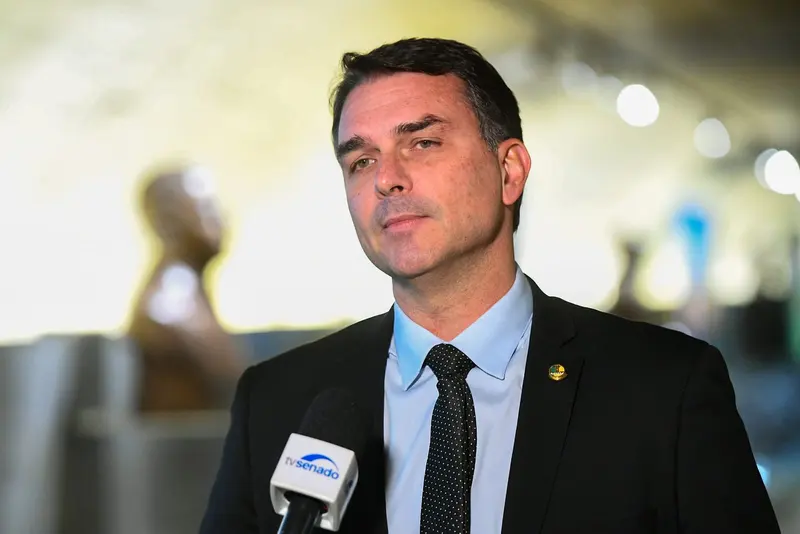 Flávio Bolsonaro, de terno escuro e gravata, fala a jornalistas no Senado