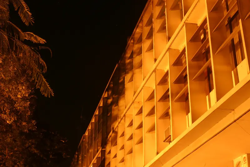 Fachada do prédio da Prefeitura de Bauru (SP), iluminada à noite, com folhagem à esquerda