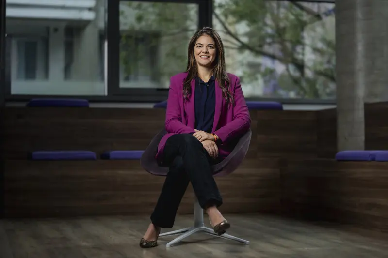 Patricia Whitaker, diretora de Investimentos do Nubank, sentada em poltrona em escritório do banco, de blazer roxo