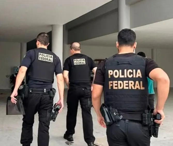 Três policiais federais, de colete preto com a inscrição Polícia Federal, entram em um prédio durante o cumprimento de mandados em Macapá