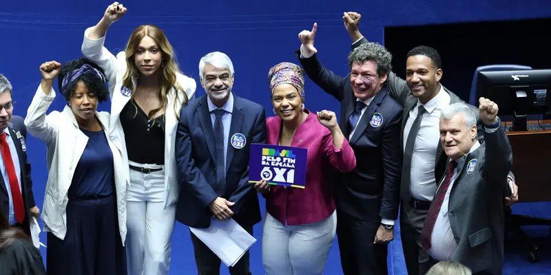 Parlamentares comemoram de punho erguido no plenário do Senado, com o cartaz Pelo fim da escala 6x1, depois da aprovação da PEC